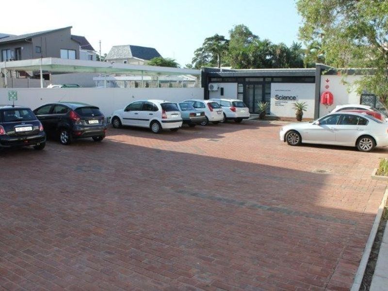 A paved exterior parking area serving the office building, featuring a perimeter wall and covered parking bays.