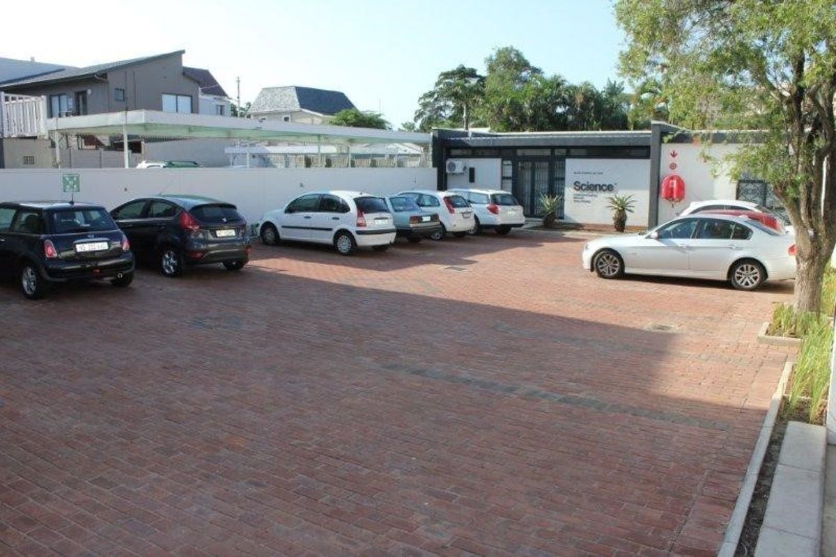 A paved exterior parking area serving the office building, featuring a perimeter wall and covered parking bays.