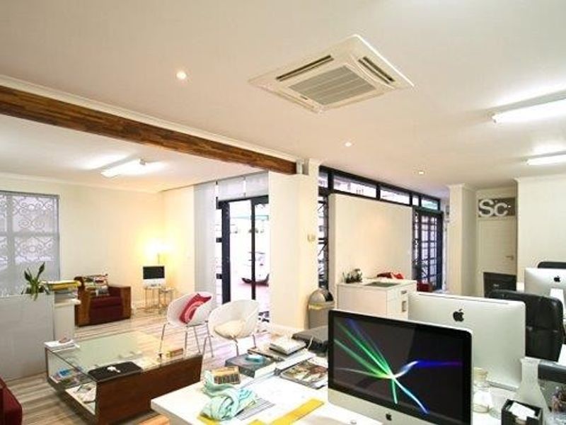 Spacious open-plan office area featuring exposed timber ceiling beams, recessed air conditioning, and large windows providing ample natural light.