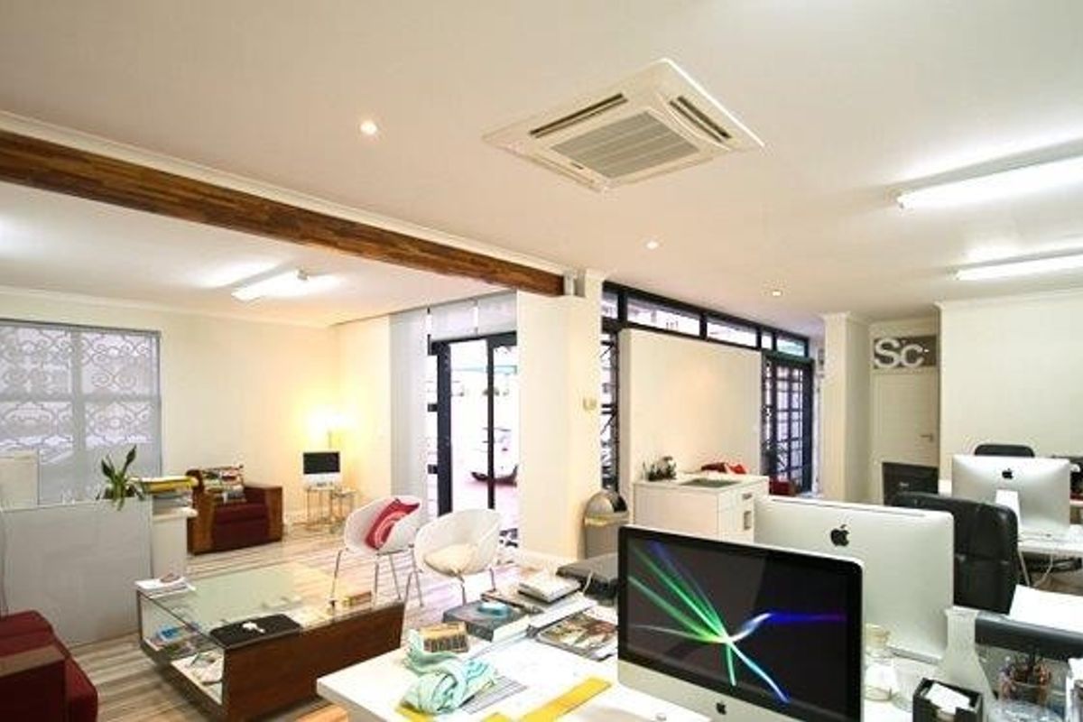 Spacious open-plan office area featuring exposed timber ceiling beams, recessed air conditioning, and large windows providing ample natural light.