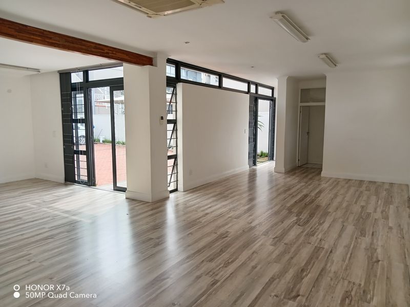 Spacious, open-plan office area featuring modern laminate flooring, large glass sliding doors providing natural light, and integrated ceiling lighting.