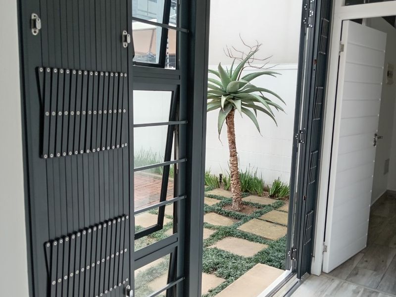 Modern office space featuring large aluminium folding doors that open onto a private paved courtyard with landscaped garden.
