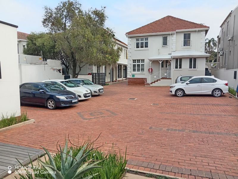 Exterior view of an office property featuring a paved parking area, brick-paved driveway, and a multi-story building with a tiled roof.