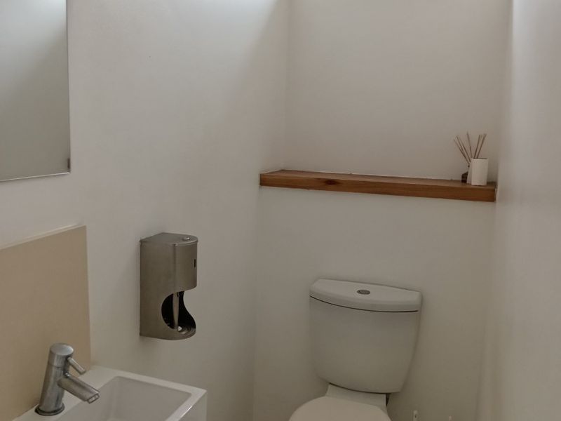 A clean and functional office restroom featuring a wall-mounted basin, toilet, tiled flooring, and a high-level window for natural light.