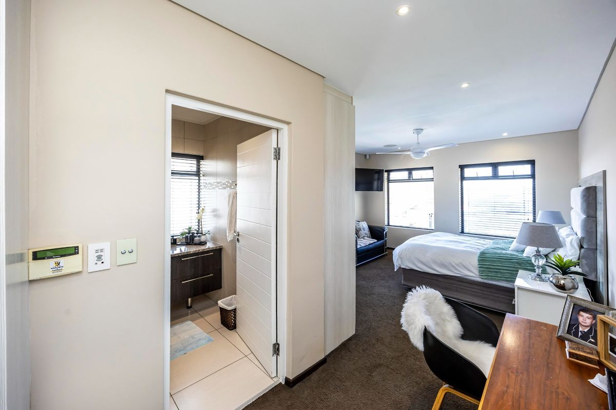 Spacious bedroom featuring an en-suite bathroom, built-in cupboards, recessed lighting, and a ceiling fan, finished with neutral tones and carpeted flooring.