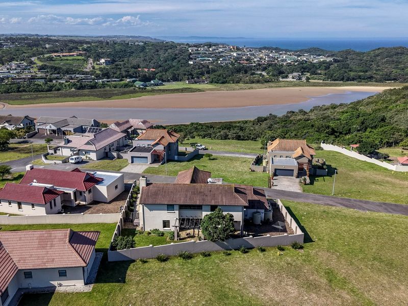 Aerial view of a residential property in a coastal estate, featuring a tiled roof house with a perimeter wall and surrounding green space.