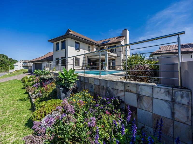 Rear view of a modern double-story house featuring a swimming pool, paved patio, and landscaped garden with a stone-tiled retaining wall and stainless steel balustrade.