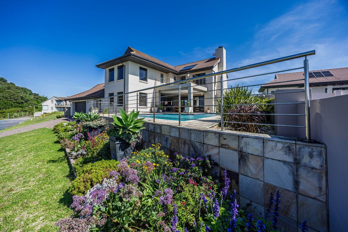 Rear view of a modern double-story house featuring a swimming pool, paved patio, and landscaped garden with a stone-tiled retaining wall and stainless steel balustrade.