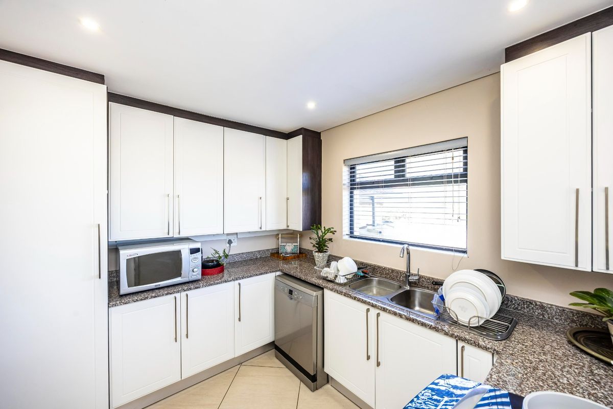 A well-maintained kitchen featuring white cabinetry, granite countertops, a double basin sink, and integrated dishwasher, complemented by recessed lighting and tiled flooring.