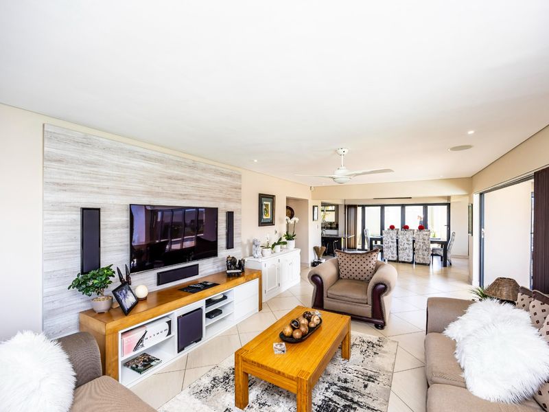 Spacious open-plan living and dining area featuring tiled floors, a modern feature wall, recessed lighting, and large sliding doors leading to the outdoor space.