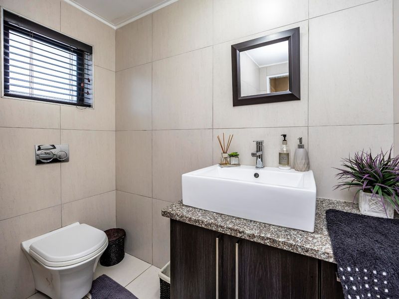 A modern bathroom featuring a wall-mounted toilet, a dark wood vanity with a granite countertop, a vessel sink, and neutral wall tiling.