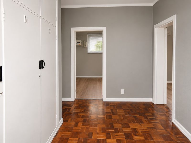A clean, empty hallway featuring classic parquet flooring and built-in storage cupboards, providing access to adjacent rooms.