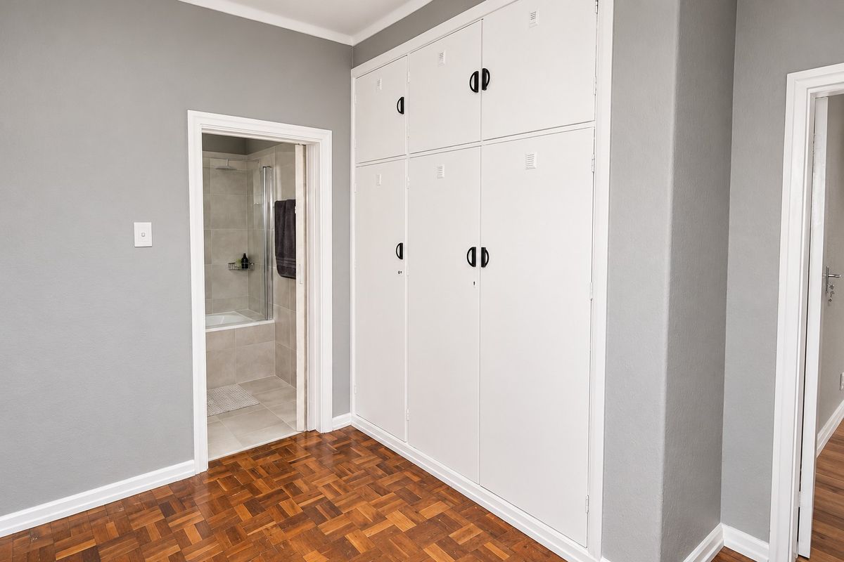 A clean bedroom featuring classic parquet flooring and extensive floor-to-ceiling built-in cupboards, with direct access to an adjoining bathroom.
