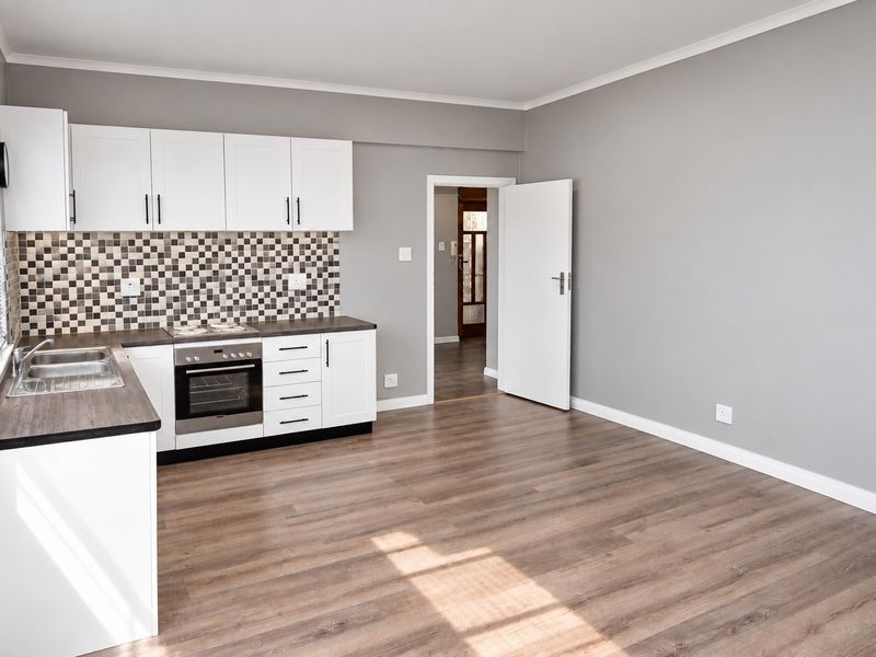 A clean, modern kitchen featuring white cabinetry, a mosaic tile backsplash, built-in oven, and wood-look laminate flooring in an open-plan layout.