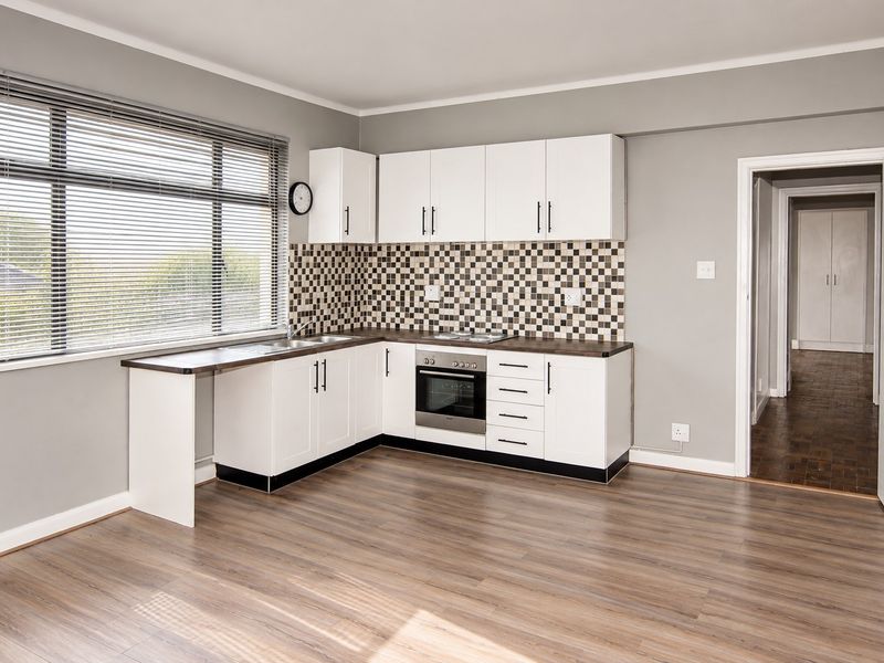 A clean, modern kitchen featuring white cabinetry, mosaic tile backsplash, built-in oven, and wood-look laminate flooring in an open-plan layout.