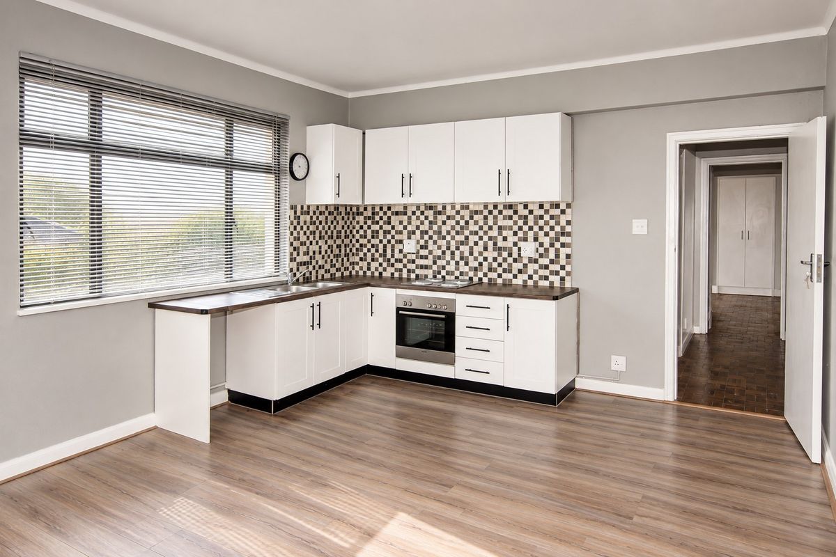 A clean, modern kitchen featuring white cabinetry, mosaic tile backsplash, built-in oven, and wood-look laminate flooring in an open-plan layout.