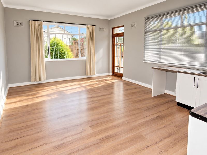 Bright and spacious open-plan living area featuring modern laminate flooring, neutral walls, and a functional kitchen corner with built-in cabinetry and sink.