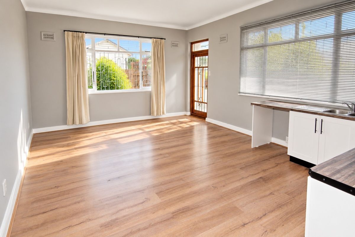 Bright and spacious open-plan living area featuring modern laminate flooring, neutral walls, and a functional kitchen corner with built-in cabinetry and sink.