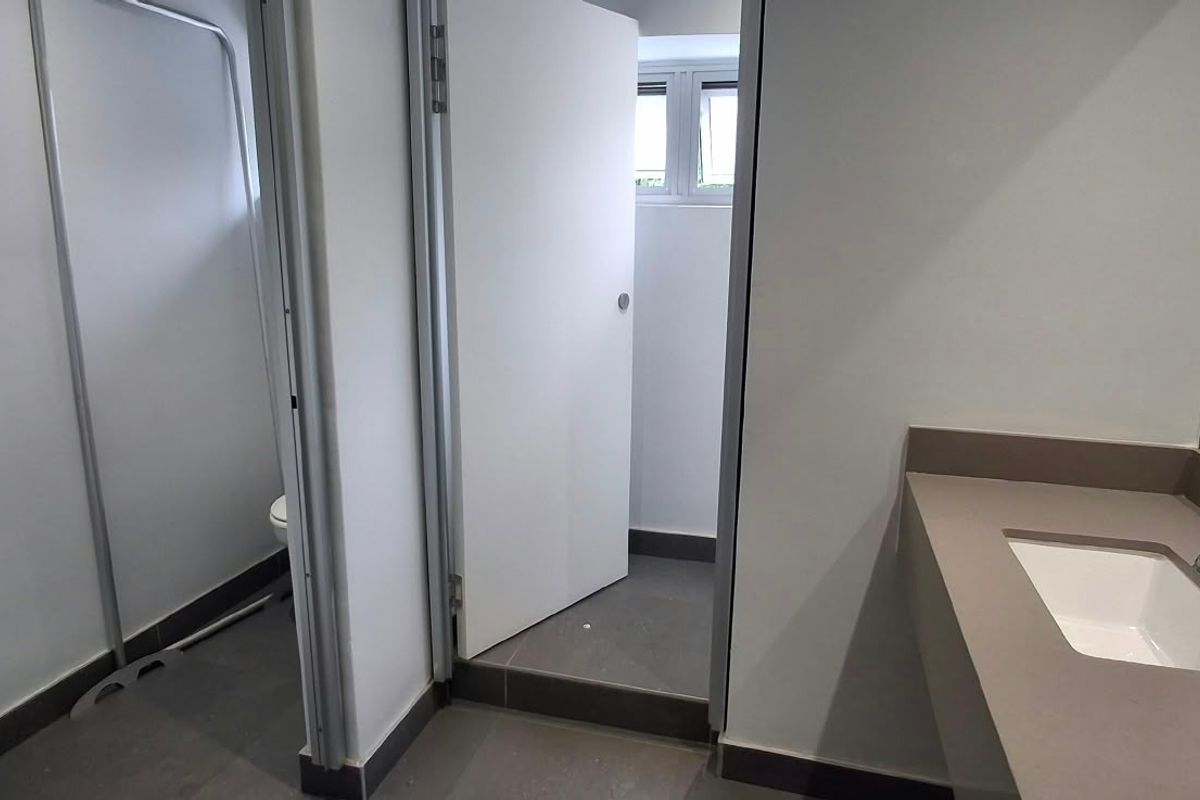 A clean, modern commercial bathroom featuring a vanity basin with a mixer tap, tiled flooring, and a separate toilet cubicle.