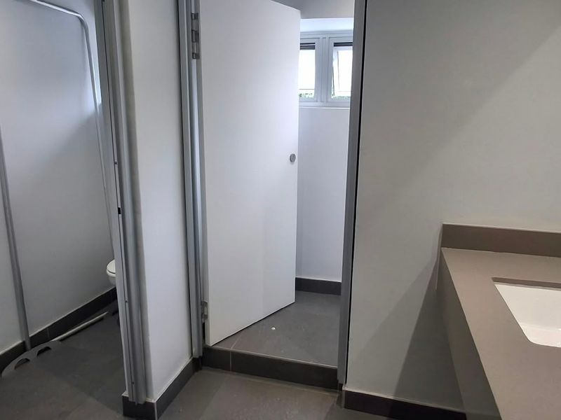 A clean, modern commercial bathroom featuring a vanity basin with a mixer tap, tiled flooring, and a separate toilet cubicle.