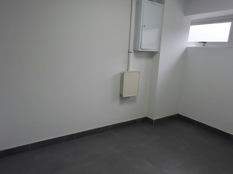 A clean, empty utility space featuring tiled flooring, high-level windows, and wall-mounted electrical distribution infrastructure.