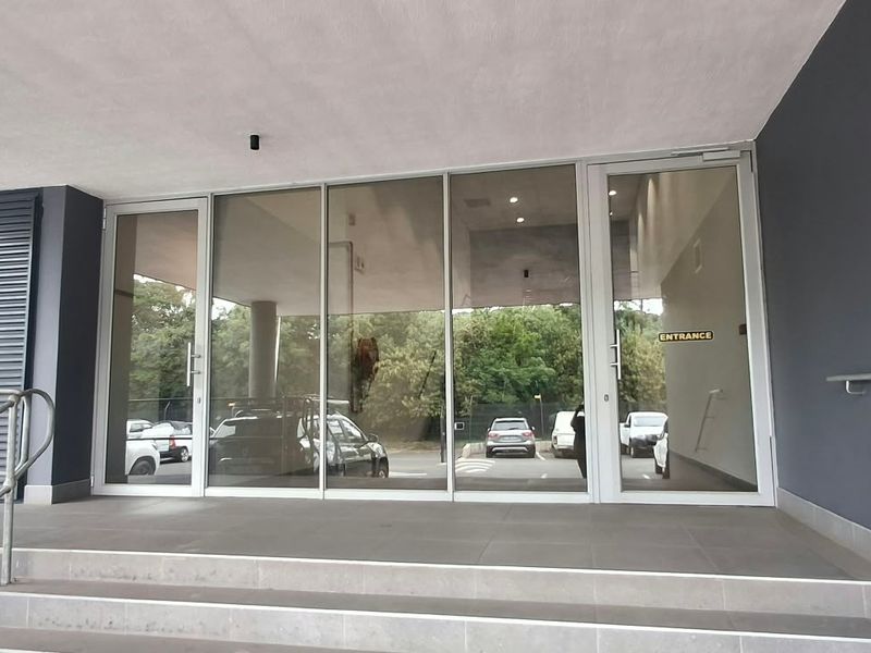 Modern commercial building entrance featuring glass doors, tiled steps, and a metal handrail, providing a clean and professional access point.