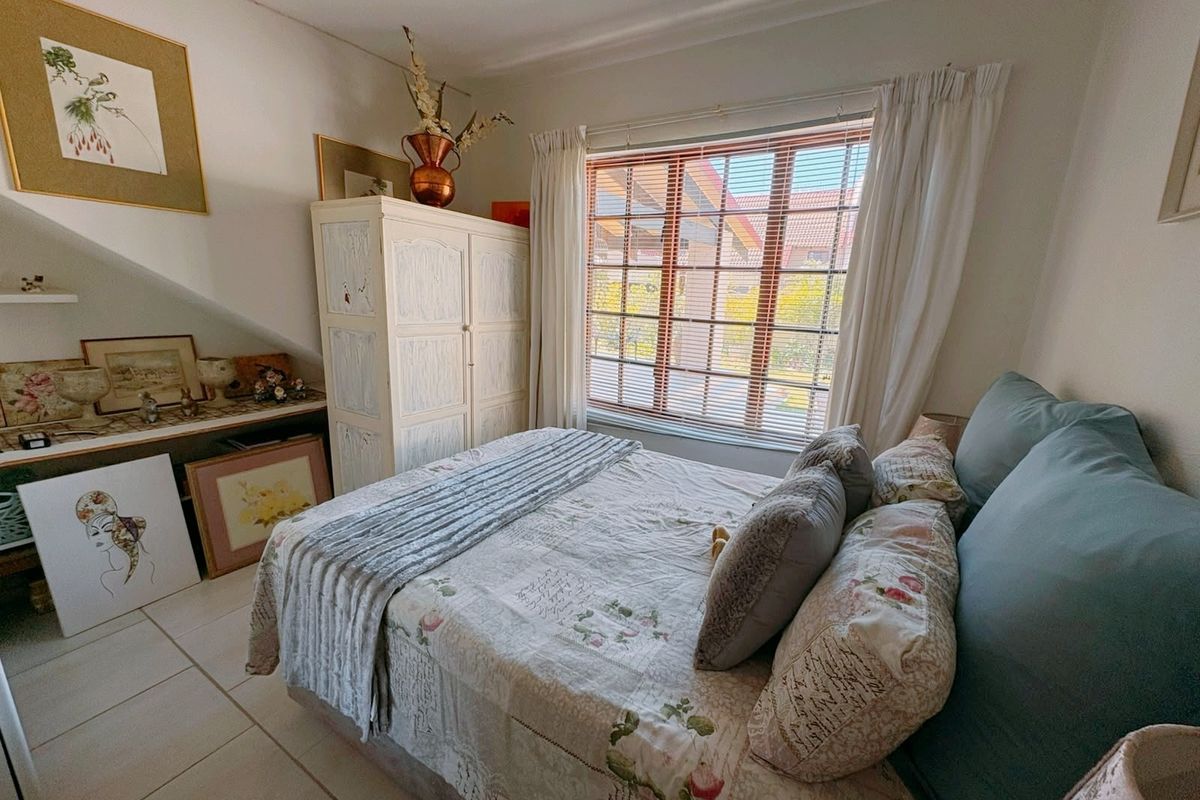 A cozy bedroom featuring tiled flooring, a window with venetian blinds, and built-in shelving under the eaves.