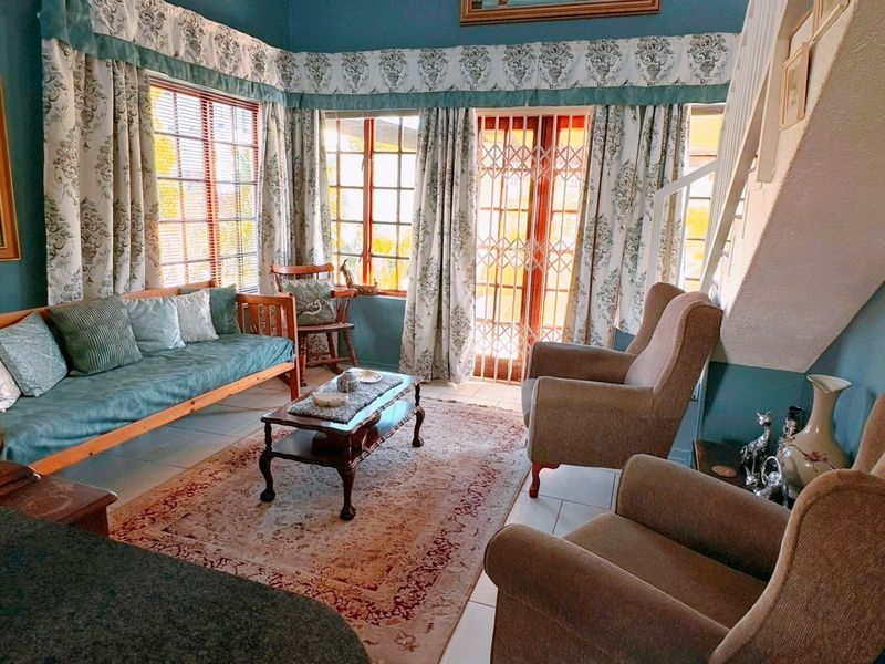 A cozy living room featuring tiled flooring, timber-framed windows, and a staircase, providing access to the outdoor area through a secure gate.
