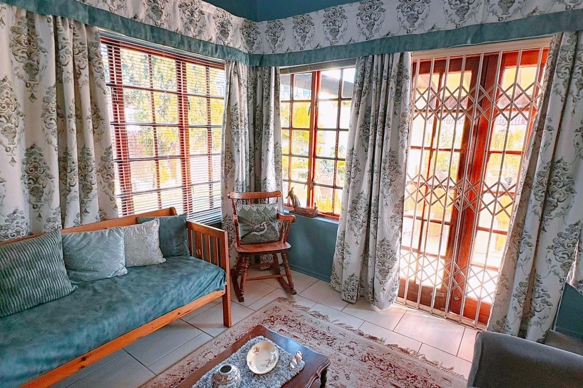 A sunlit living room featuring tiled flooring, timber-framed windows, and a secure metal gate leading to the outdoor area.