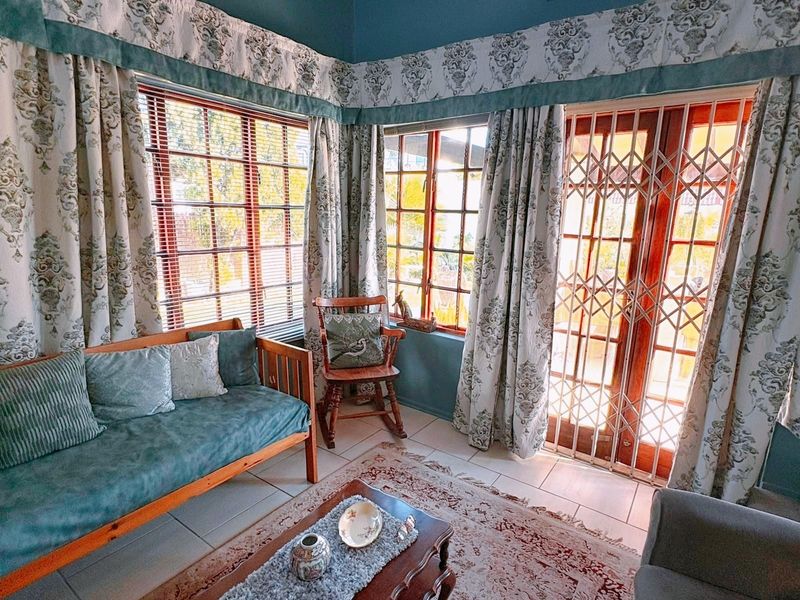 A sunlit living room featuring tiled flooring, timber-framed windows, and a secure metal gate leading to the outdoor area.