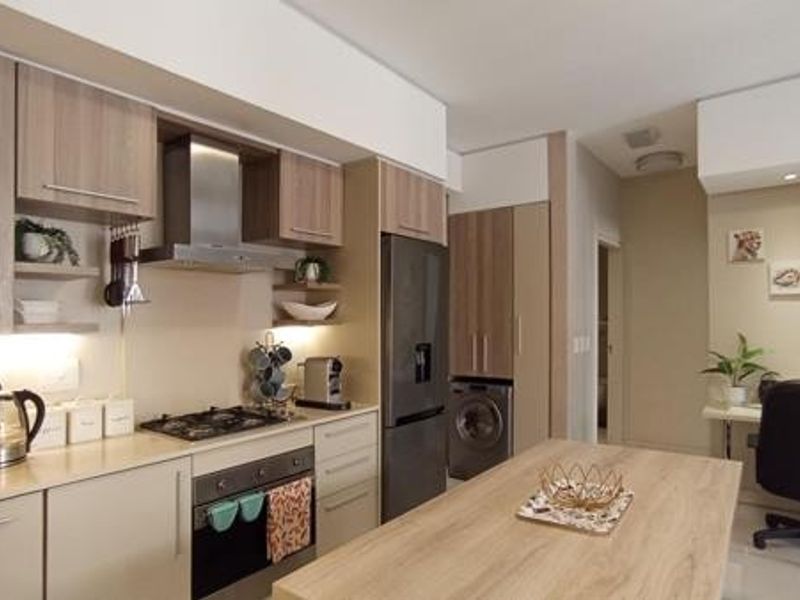 Modern kitchen featuring light wood cabinetry, stone countertops, integrated appliances, a gas hob, and a functional kitchen island with an adjacent workspace area.