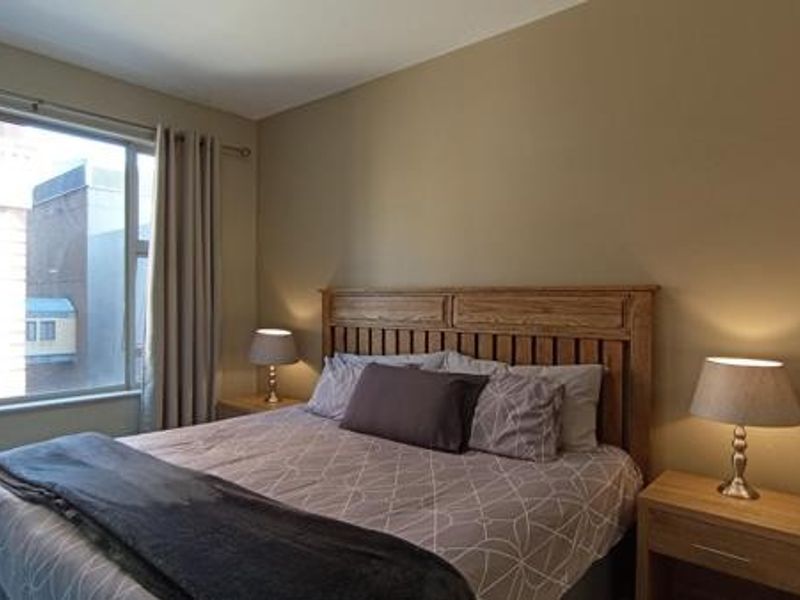 A well-lit bedroom featuring a large window with neutral wall tones and a functional layout.