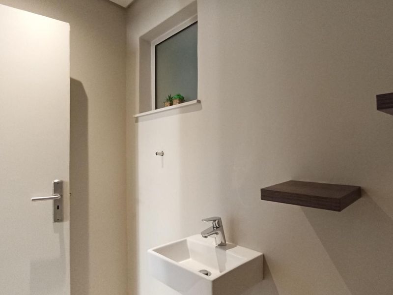 A clean and minimalist guest bathroom featuring a wall-mounted basin with a chrome mixer tap and floating wooden shelves.