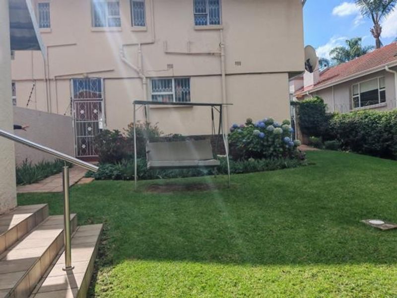 A rear exterior view of the property featuring a well-maintained lawn, landscaped garden beds, and tiled steps with a stainless steel handrail.