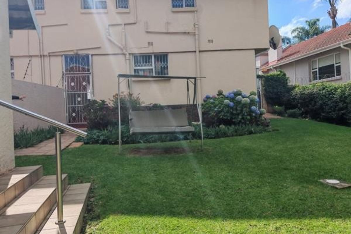 A rear exterior view of the property featuring a well-maintained lawn, landscaped garden beds, and tiled steps with a stainless steel handrail.