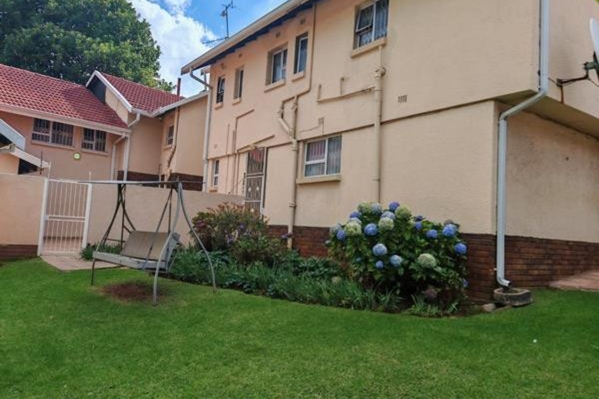 Rear view of the property featuring a lawn, garden bed, and plastered exterior walls with visible downpipes and window frames.