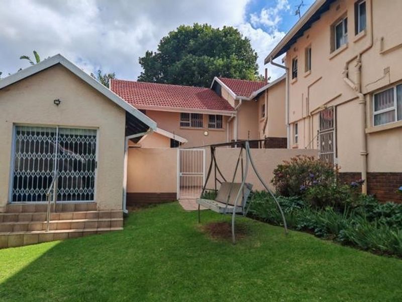 Rear view of the property featuring a small lawn area, security gates, and multi-level building structure with tiled roofing.