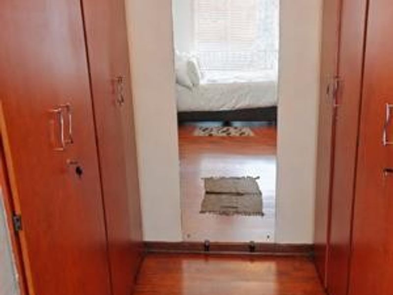A bedroom dressing area featuring extensive built-in wooden cupboards and laminate flooring, providing ample storage space.