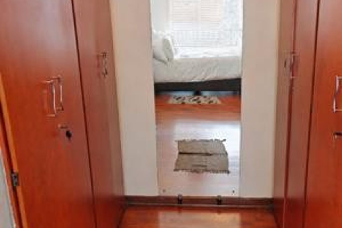 A bedroom dressing area featuring extensive built-in wooden cupboards and laminate flooring, providing ample storage space.