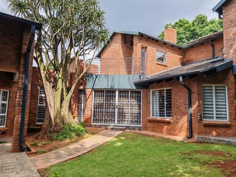 Rear view of a face brick house featuring a paved walkway, established tree, and a balcony with metal railings.