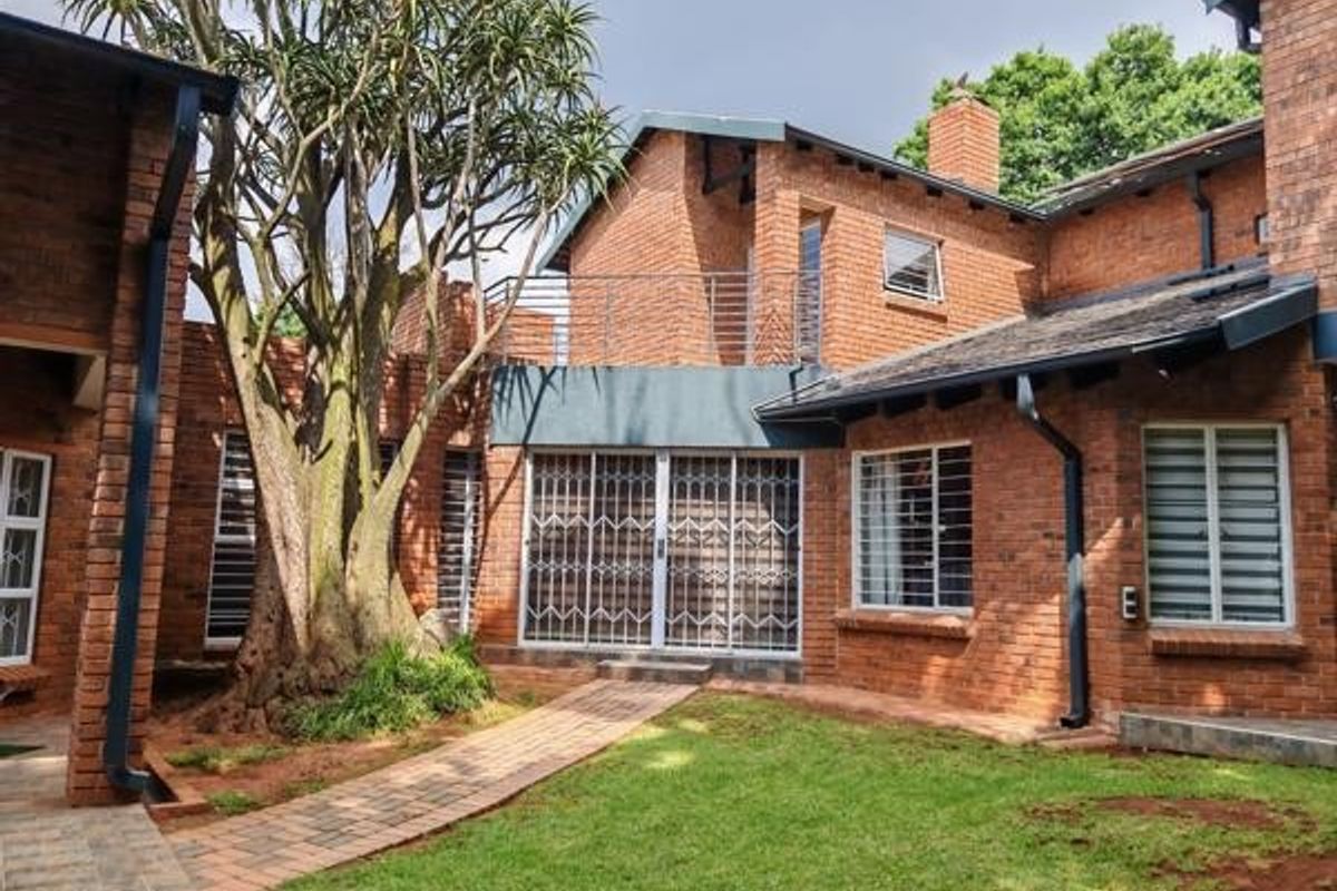 Rear view of a face brick house featuring a paved walkway, established tree, and a balcony with metal railings.