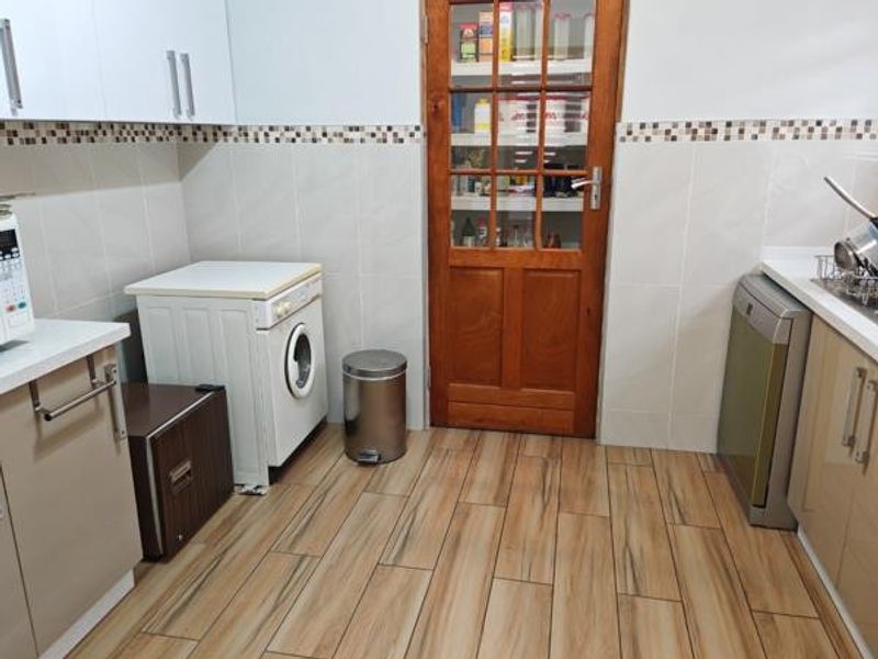 A functional scullery area featuring tiled flooring, tiled splashbacks, built-in cabinetry, and a classic timber door with glass panels.