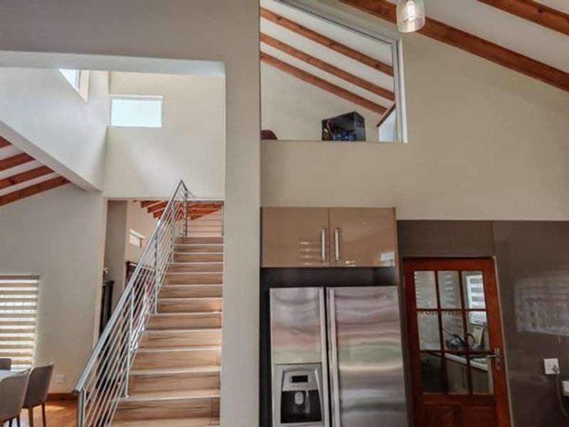 Open plan living area featuring a striking staircase with stainless steel balustrade, exposed timber ceiling beams, and a mezzanine level with vaulted ceilings.