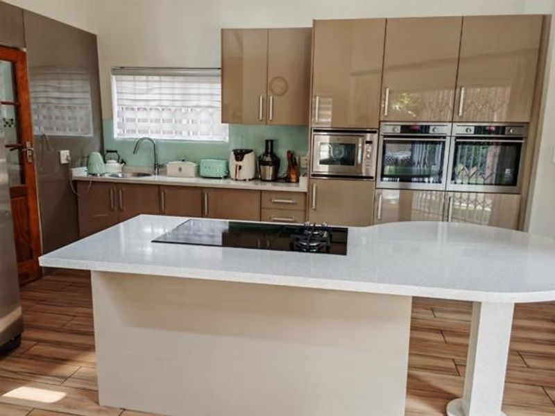 Modern kitchen featuring high-gloss cabinetry, a central island with an integrated hob, stone countertops, and built-in double ovens.