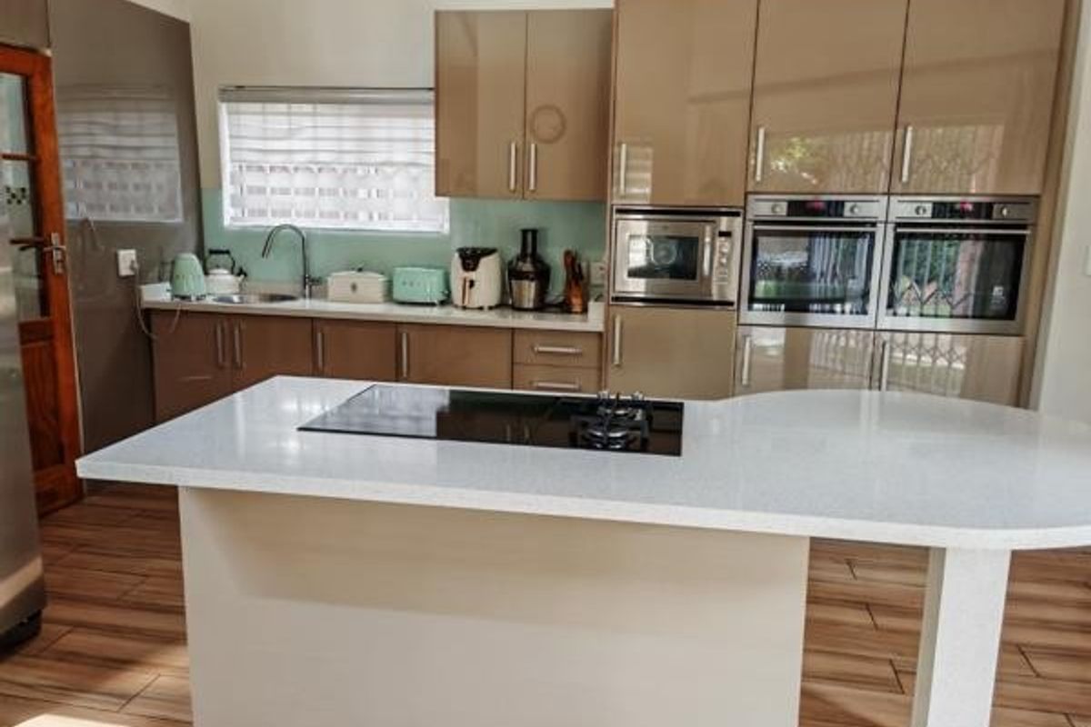 Modern kitchen featuring high-gloss cabinetry, a central island with an integrated hob, stone countertops, and built-in double ovens.