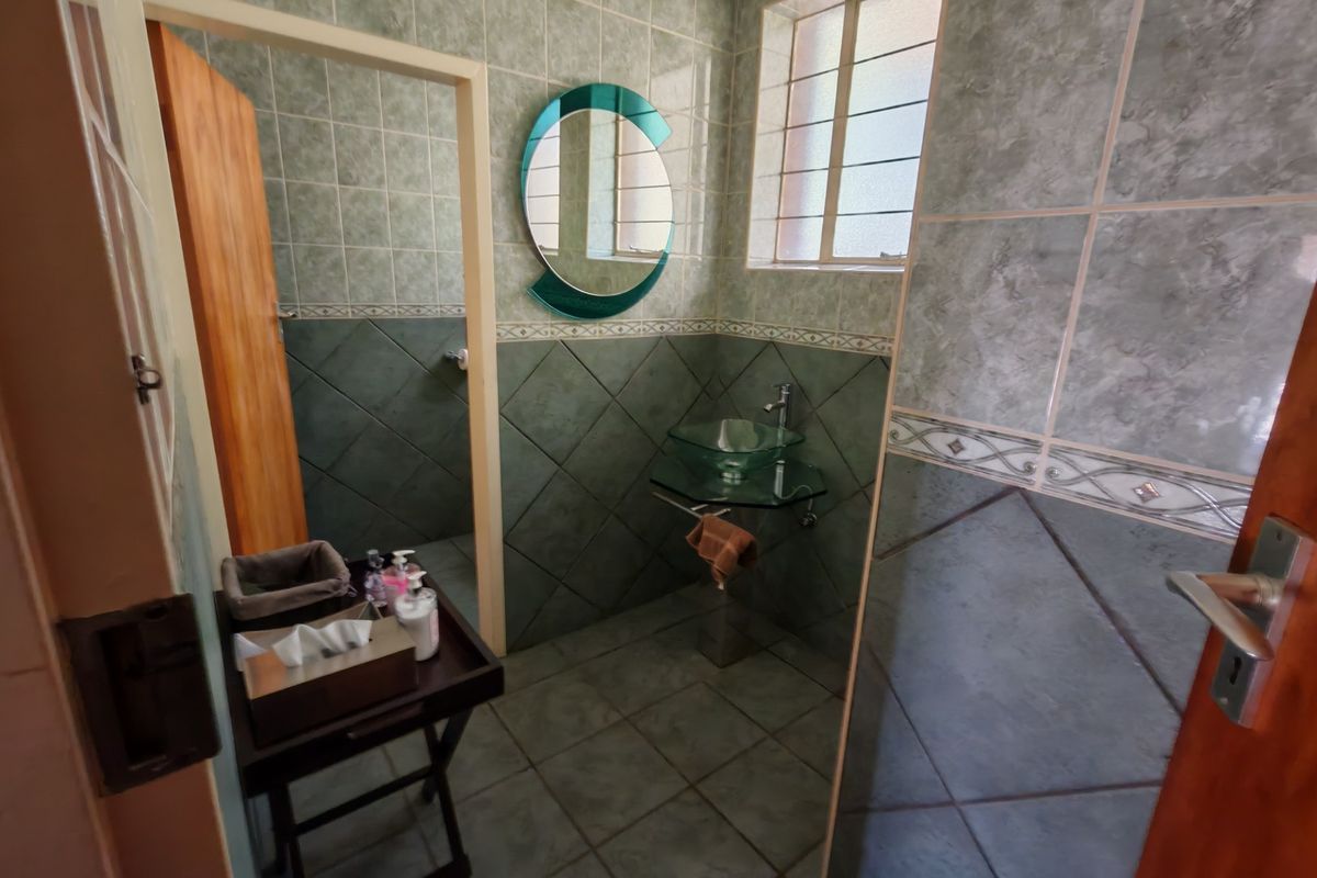 A compact bathroom featuring tiled walls and flooring, a glass vessel sink with a pedestal vanity, and a window with security bars.