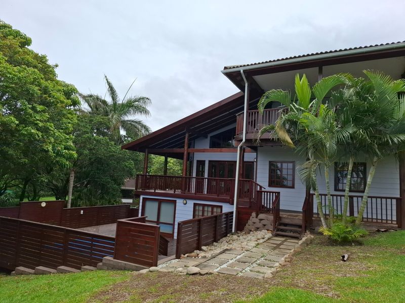 Rear view of a multi-level home featuring timber decking, a swimming pool, and a stone pathway set within a landscaped garden.