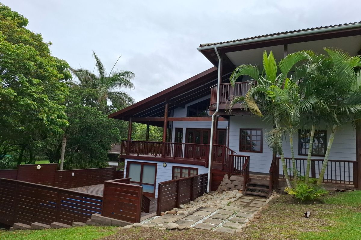 Rear view of a multi-level home featuring timber decking, a swimming pool, and a stone pathway set within a landscaped garden.