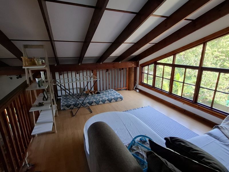 Loft-style bedroom featuring exposed timber ceiling beams, laminate flooring, and large windows providing natural light and garden views.