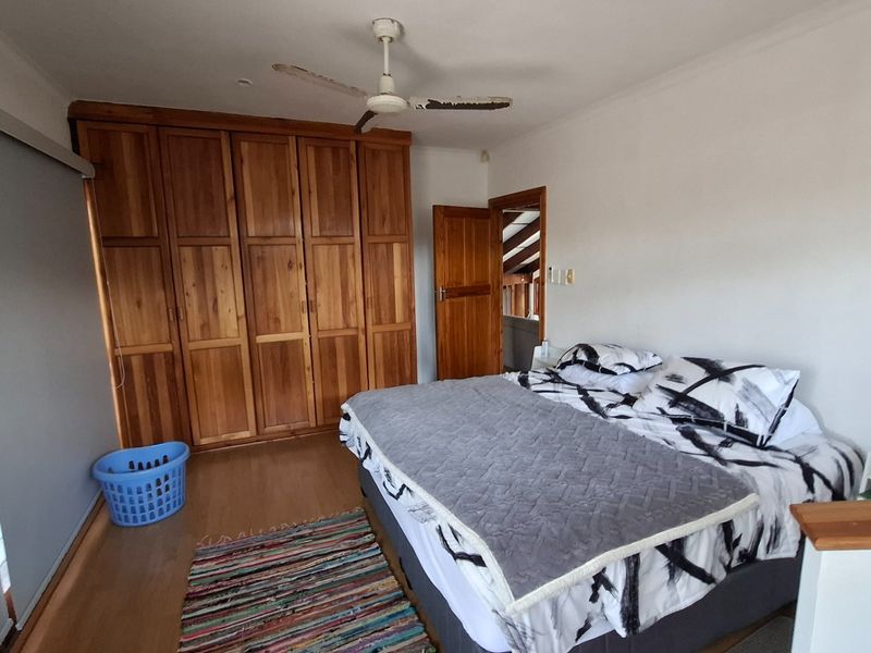 A bedroom featuring built-in wooden cupboards, laminate flooring, and a ceiling fan, offering a functional space with potential for cosmetic updates.